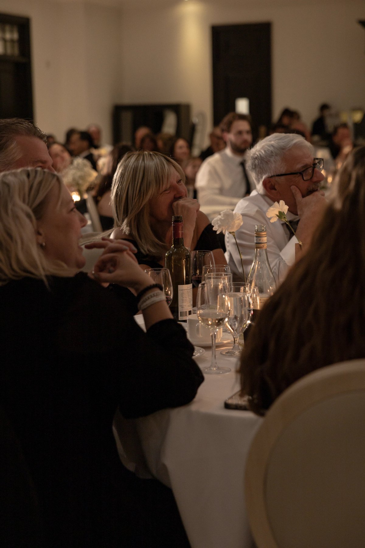 mother of groom emotionally listending to speeches during dimly lit dinner reception