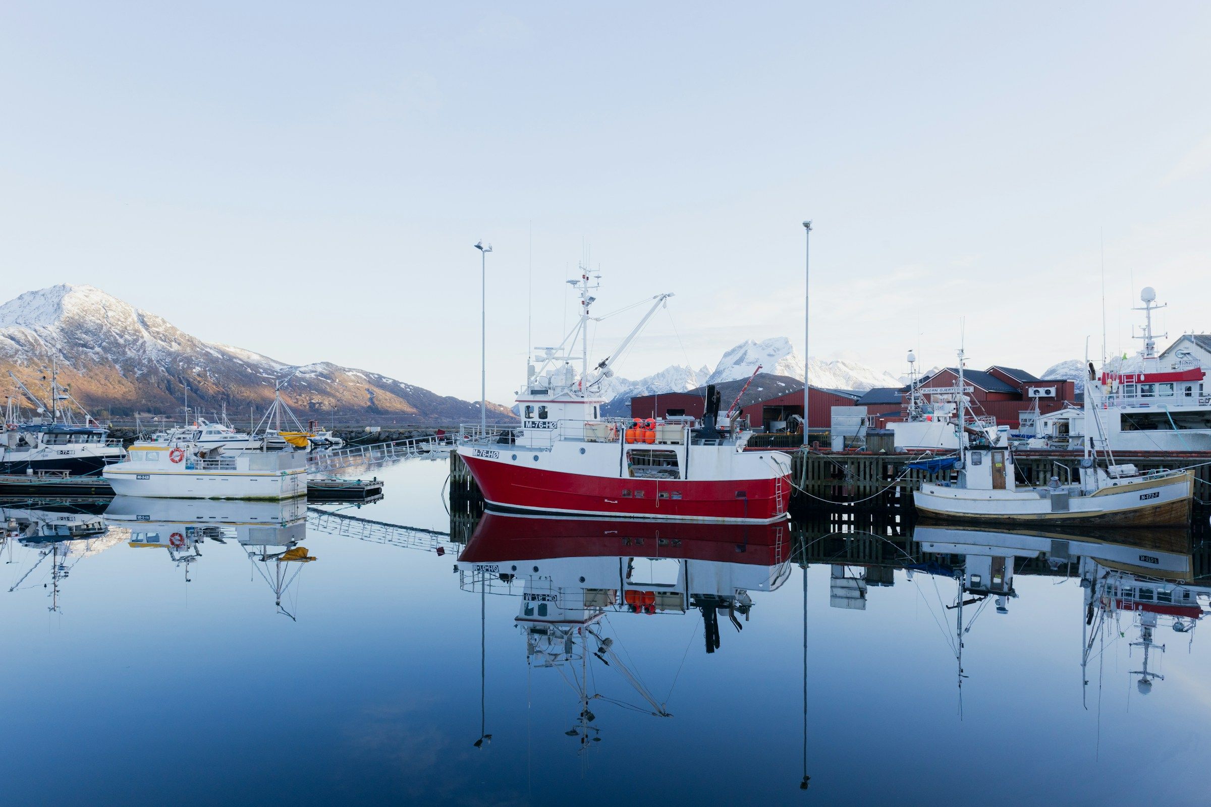 Fiskefartøy ved kai med fjell og speilinger i stille vann.