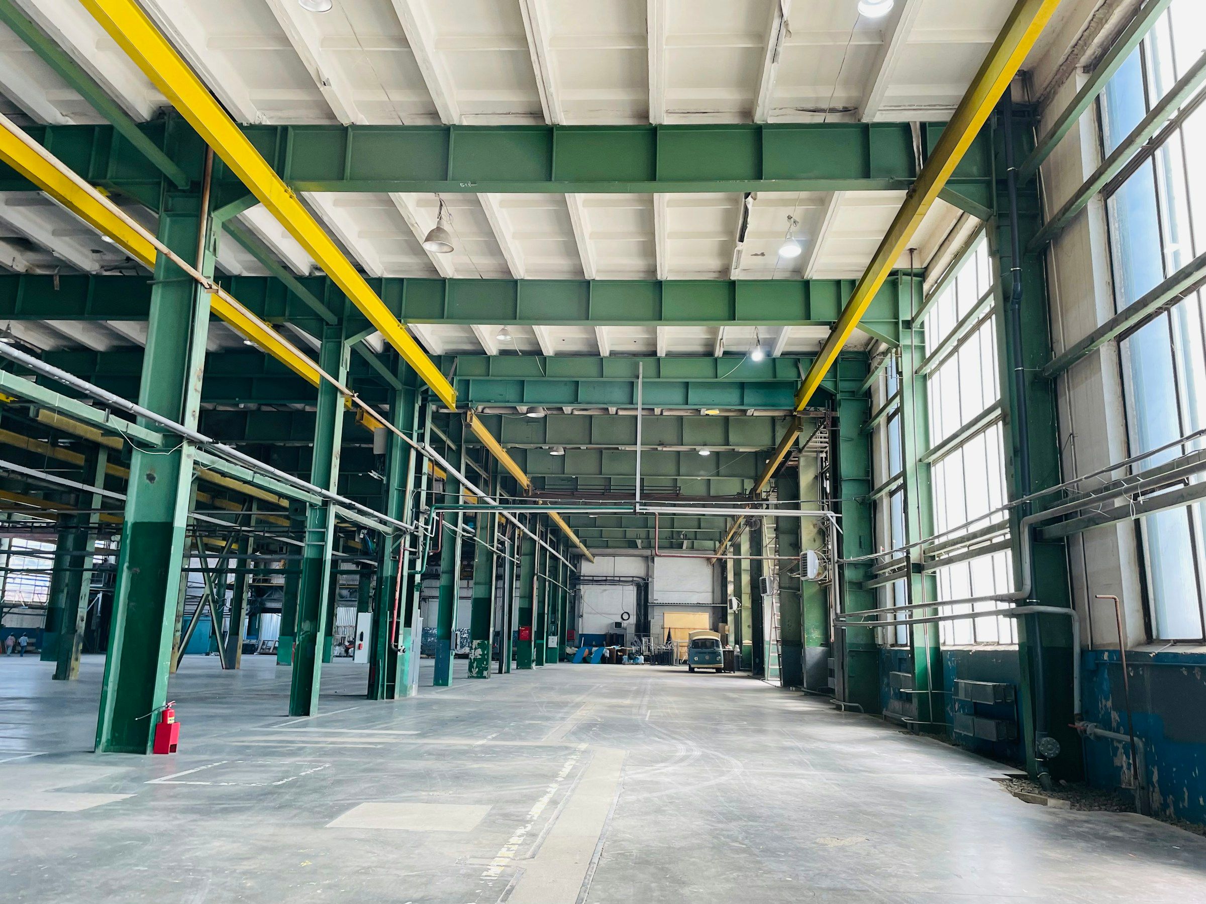Åpen industrihall med bæresøyler, traverskraner og store vinduer.