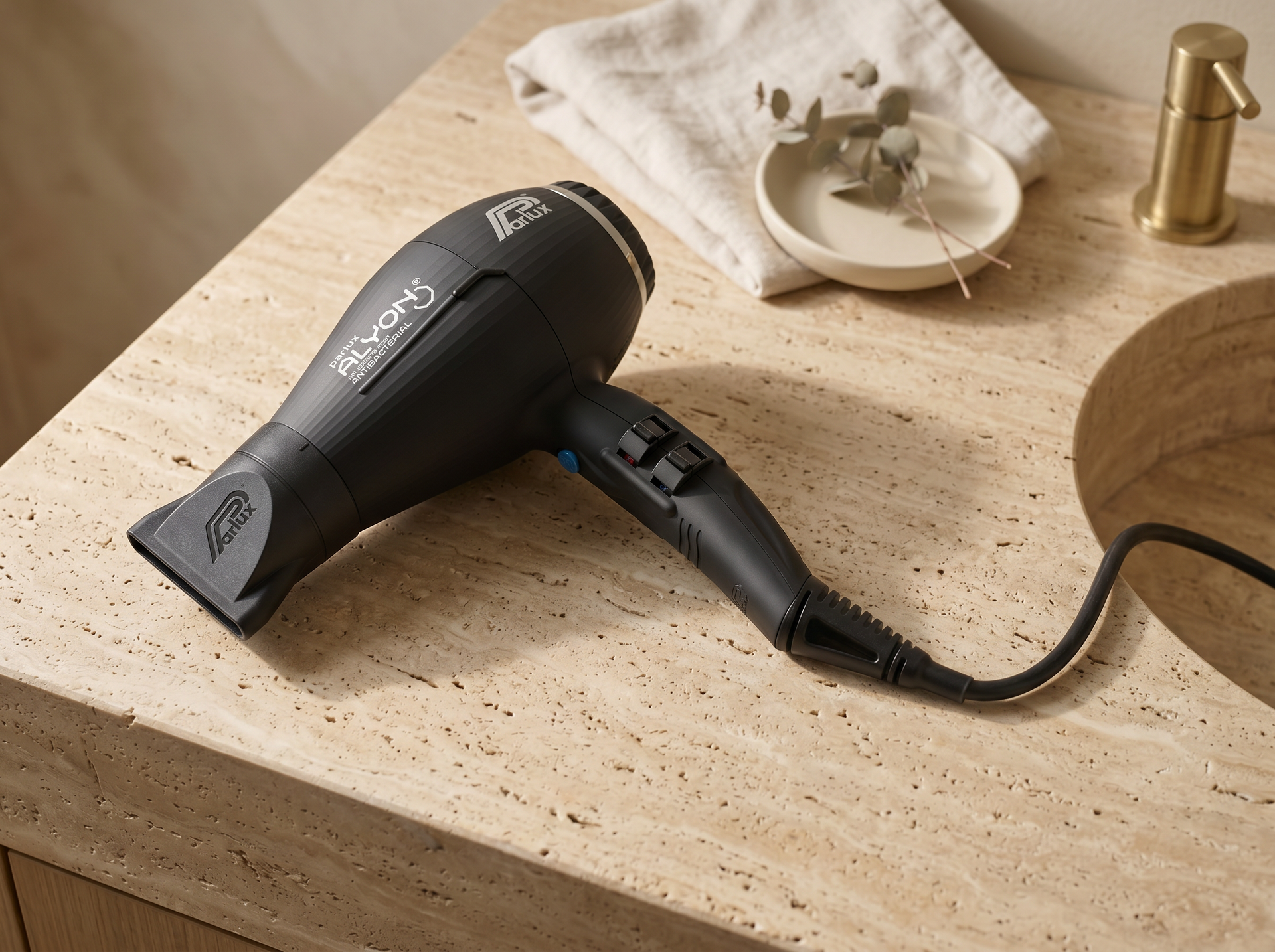 Parlux Alyon Air Ionizer liegt flach auf einer warmen Travertin-Salon-Konsole neben gefaltetem Leinen-Handtuch und Eukalyptus-Zweig in Keramikschale