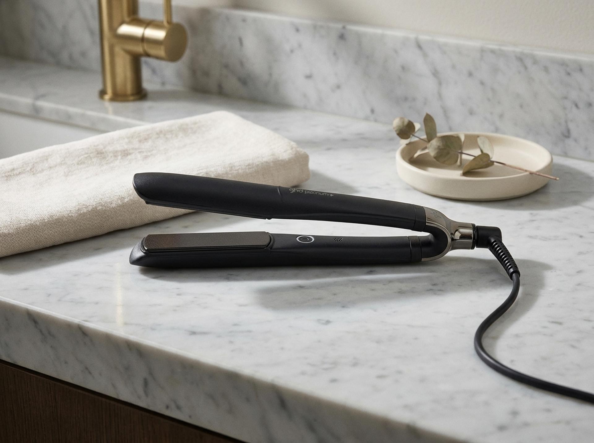 ghd Platinum+ Styler liegt flach auf einer hellen Marmor-Salon-Konsole neben einer gefalteten Leinen-Serviette und einer kleinen Keramikschale