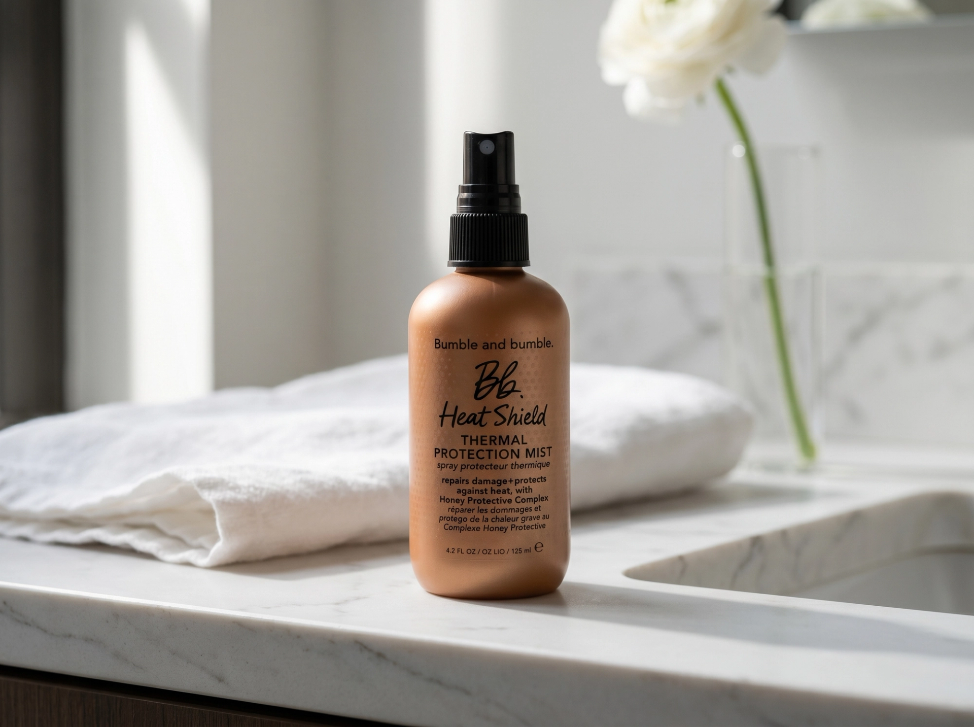 Editorial Scene: Bumble and Bumble Heat Shield Mist auf matte-white-stone-Vanity in modernem NYC-Loft, gefaltetes weißes Leinentuch und einzelne weiße Blüte in schlanker Glasvase im Bokeh, NYC Editorial Morning Light – Premium-Mockup