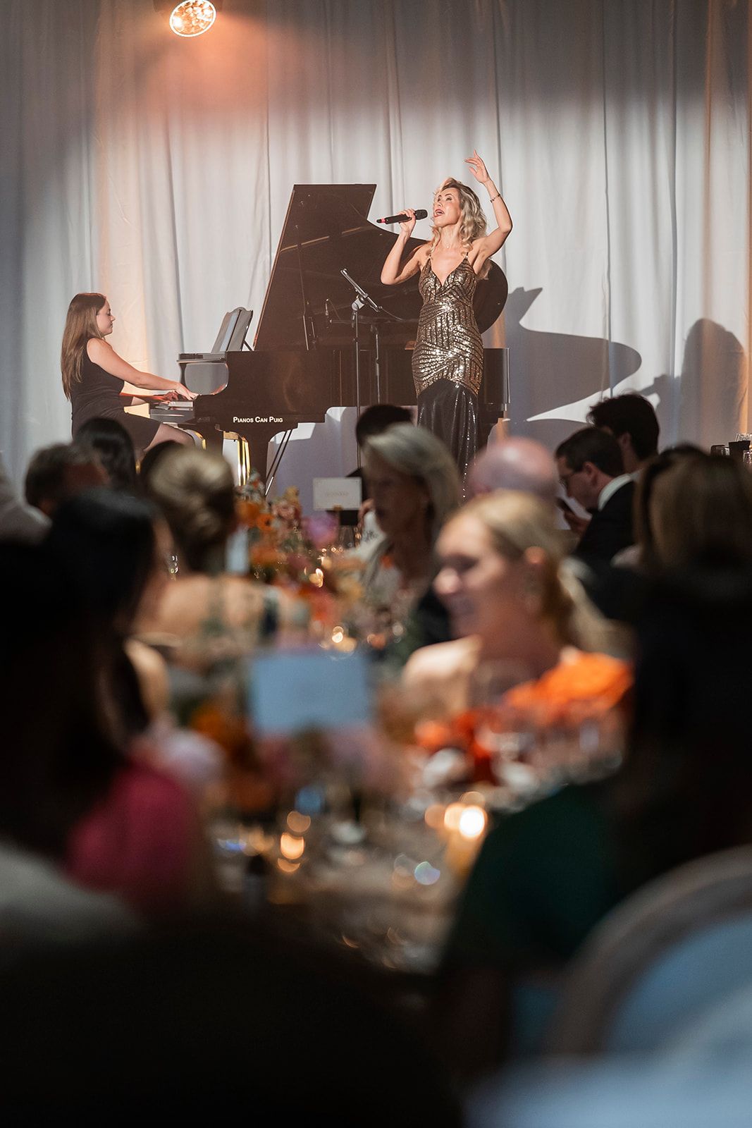 Singer performing beside a grand piano before an audience