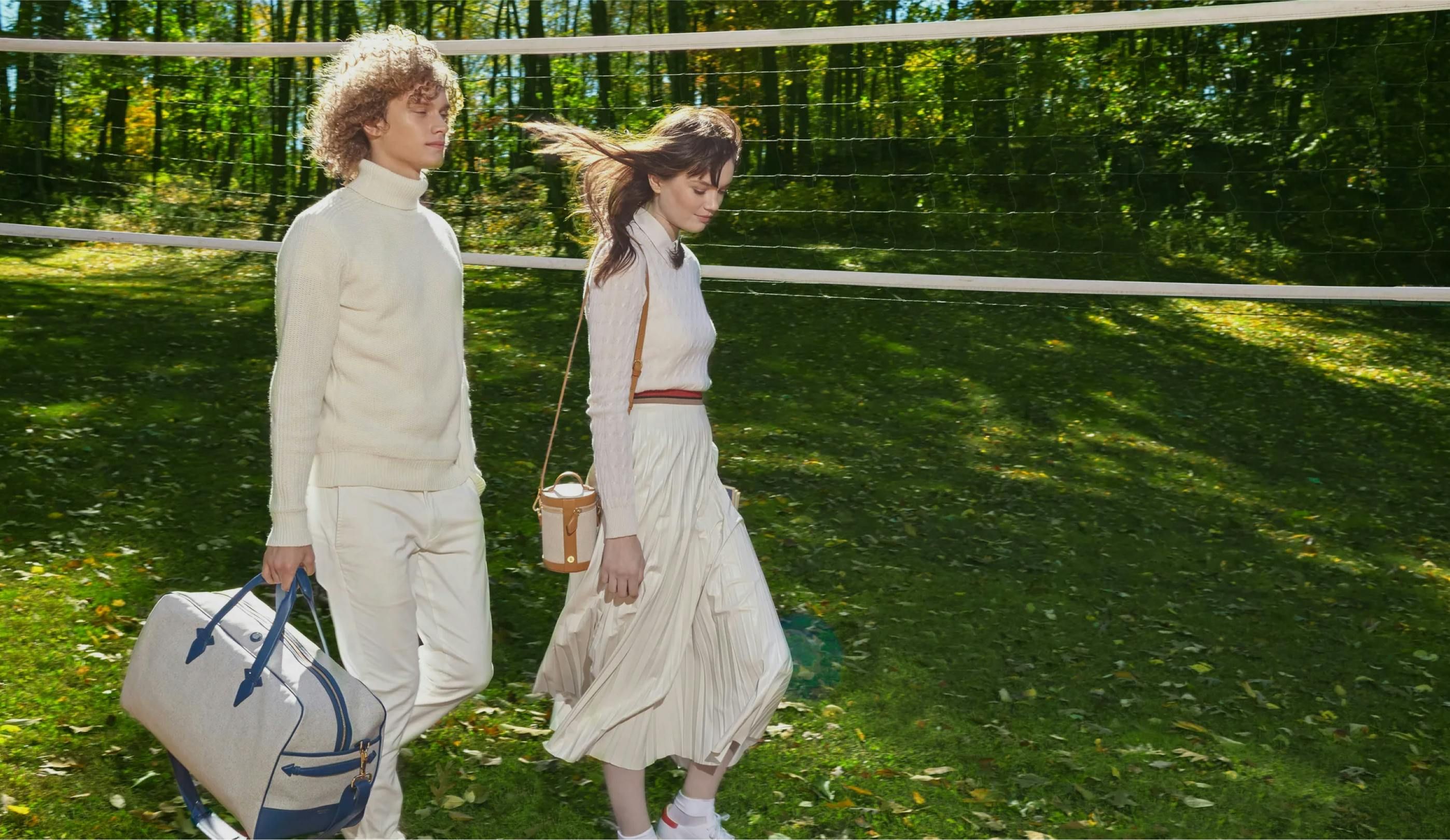 A man and woman walking on a grass volleyball court with their Paravel bags