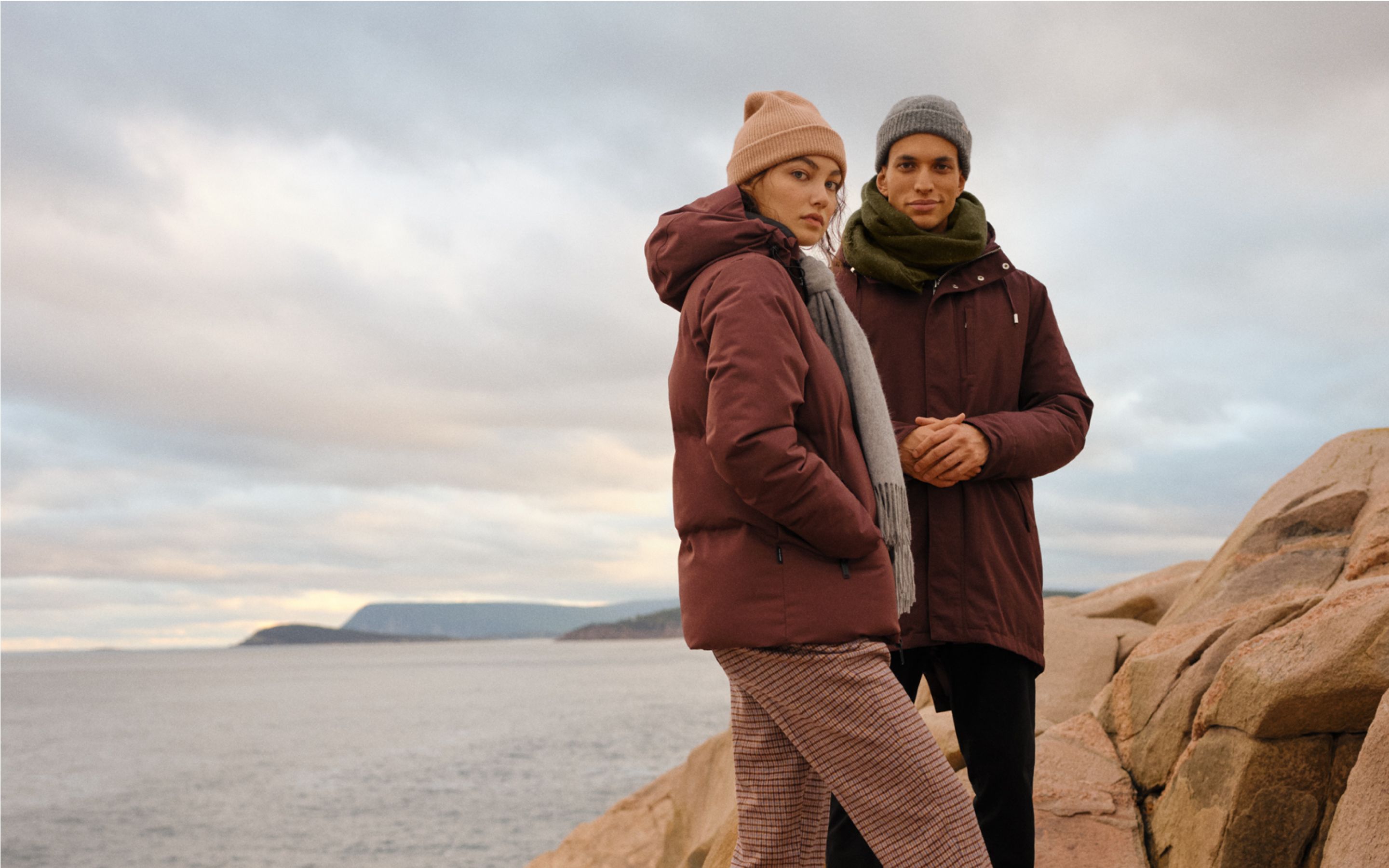 A man and woman on a cliff at the ocean wearing Frank & Oak