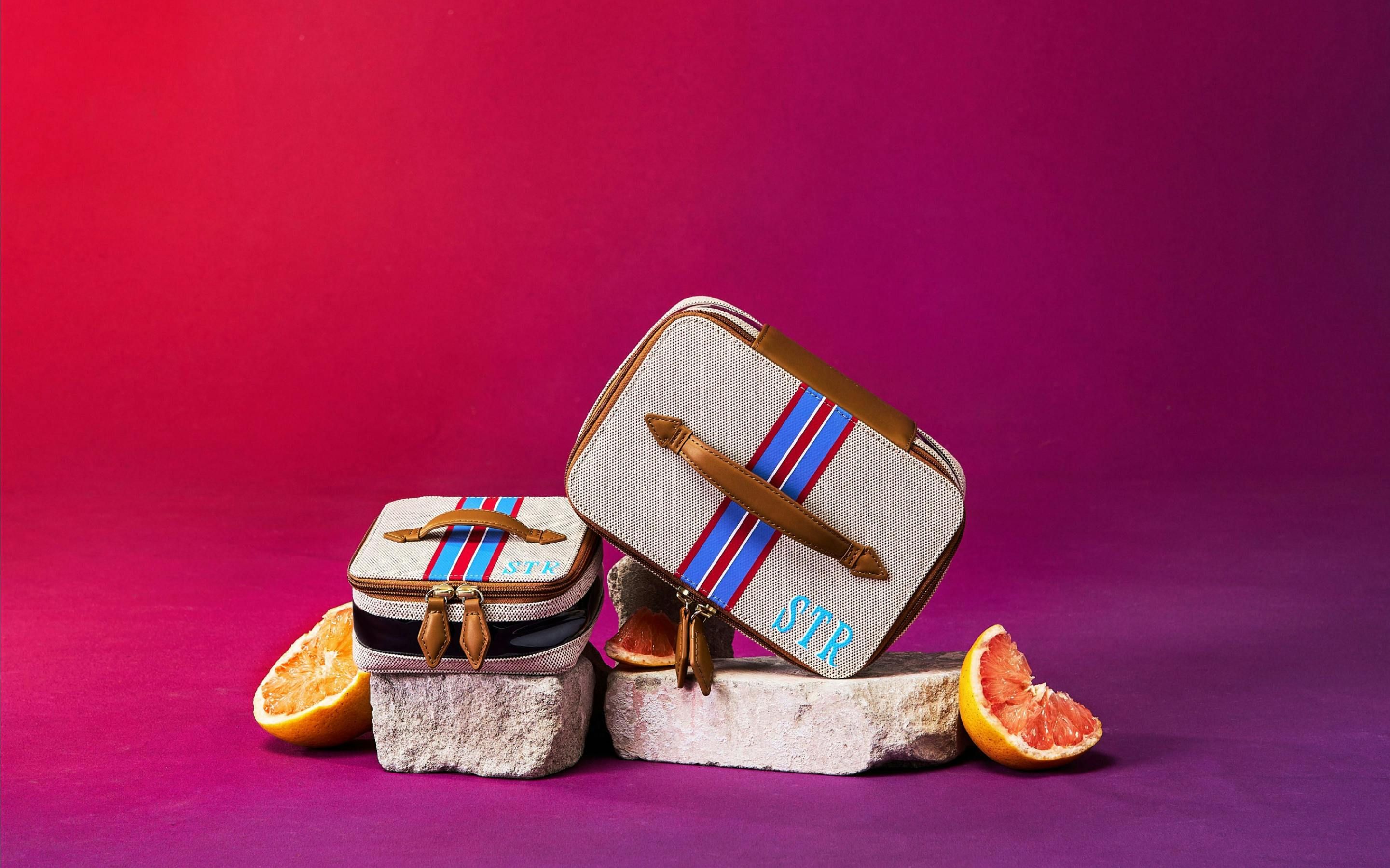 Two embroidered Paravel bags sitting on rocks shot on a gradient background with orange slices