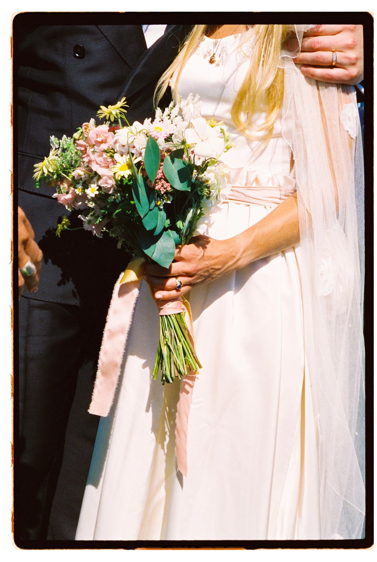 Film photograph close-up of a bride's dress and bouquet tied with pink ribbon
