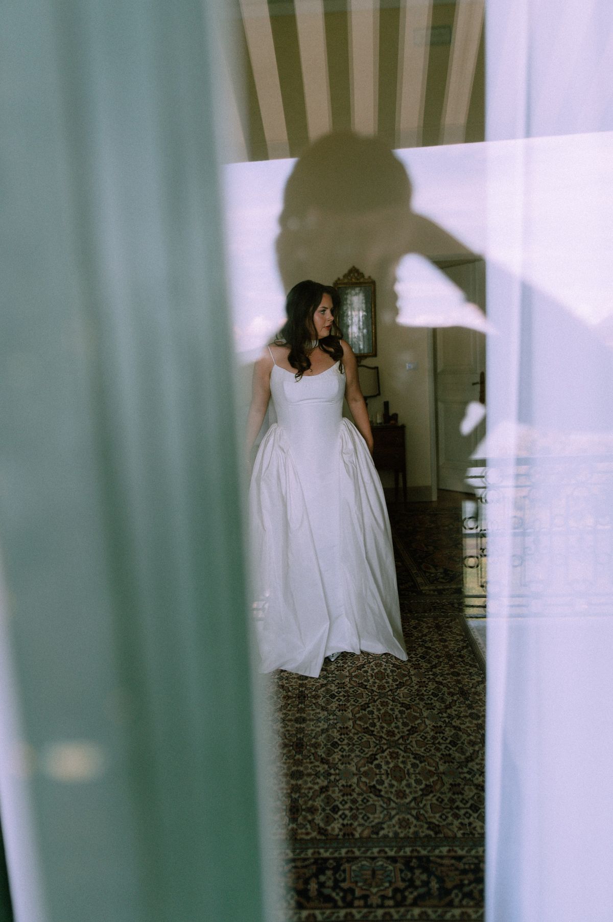 Bride in a vintage inspired taffeta dress seen through a window