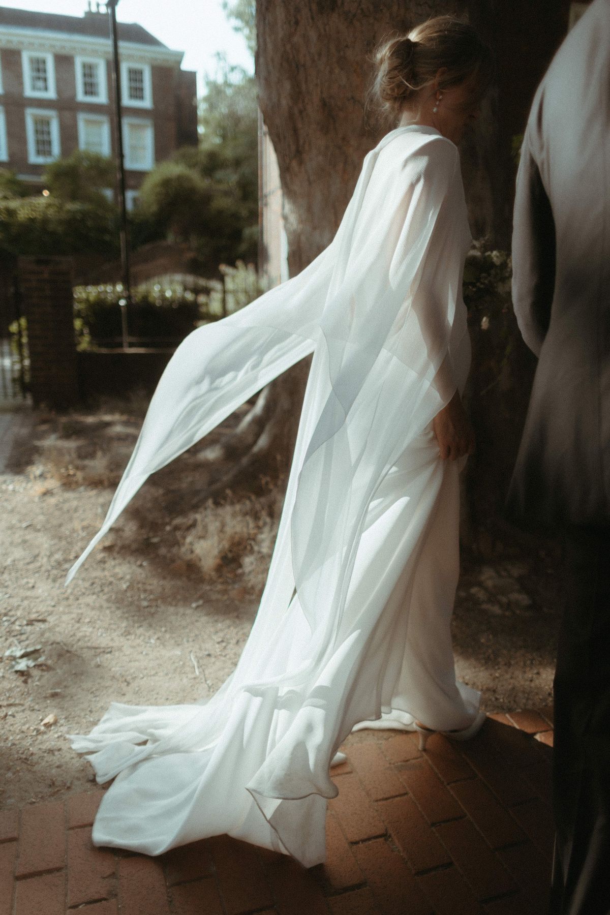 Bride in a silk chiffon cape billowing in the wind beneath a tree