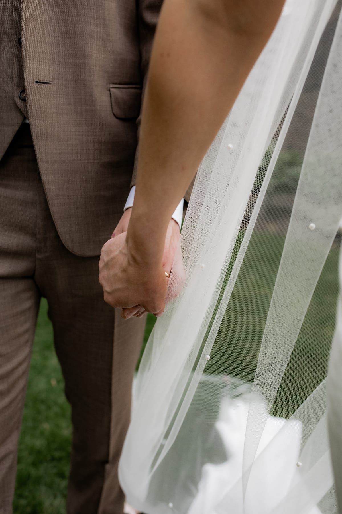 Intimate moment of bride and groom holding hands with veil