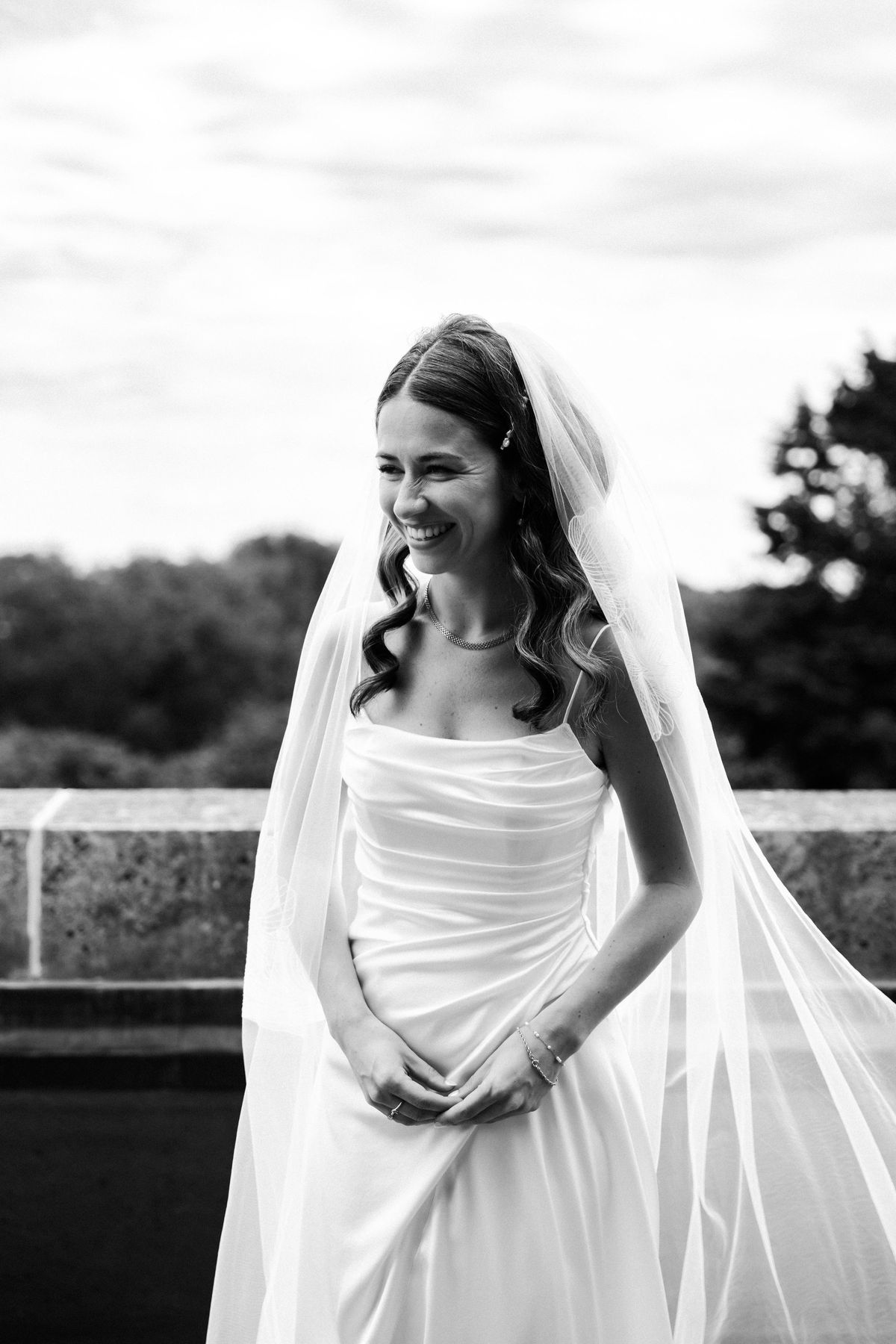 Black and white portrait of a smiling bride in a draped satin dress and long tulle veil