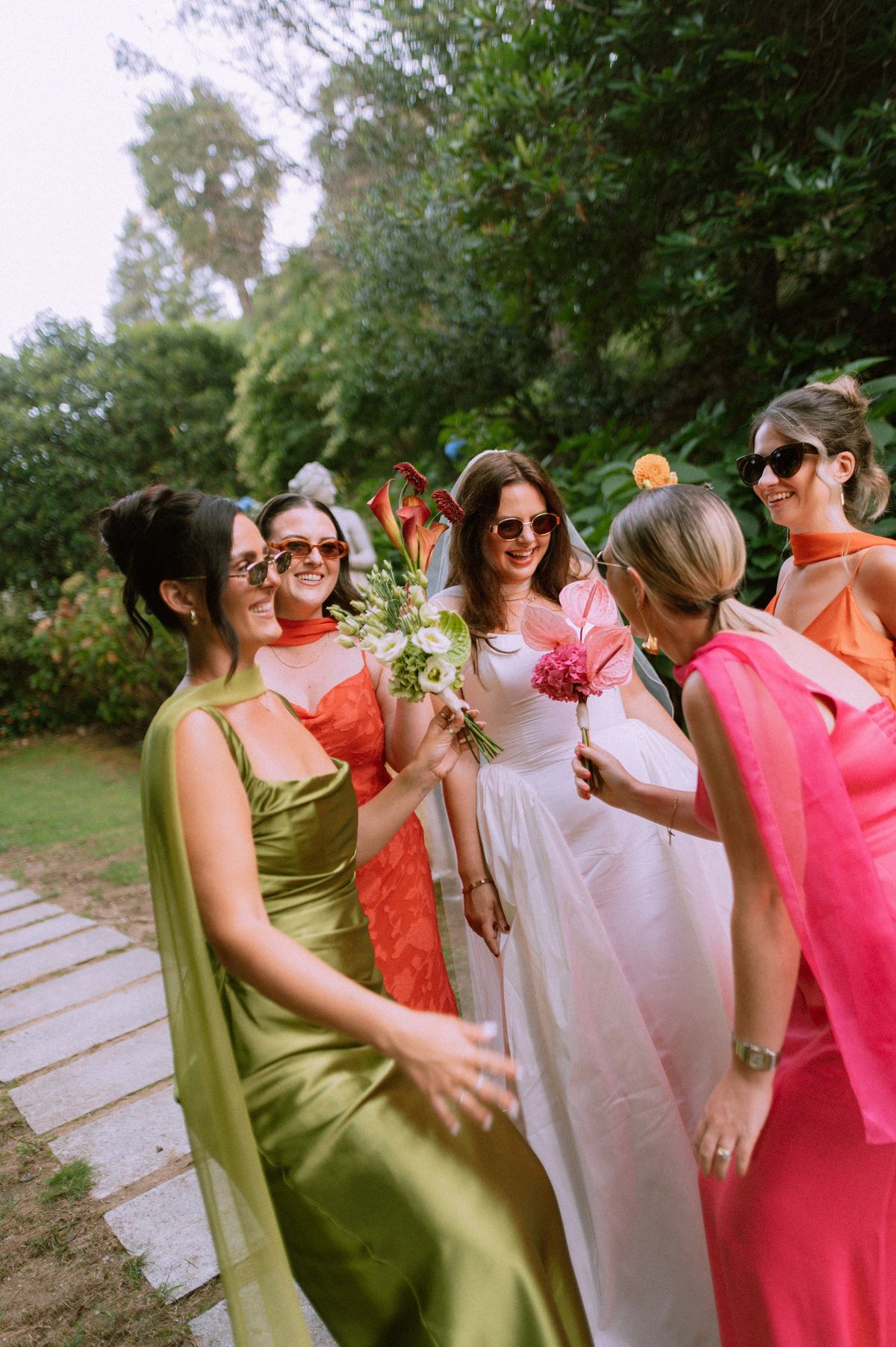 Bride laughing with bridesmaids in bright dresses in a garden
