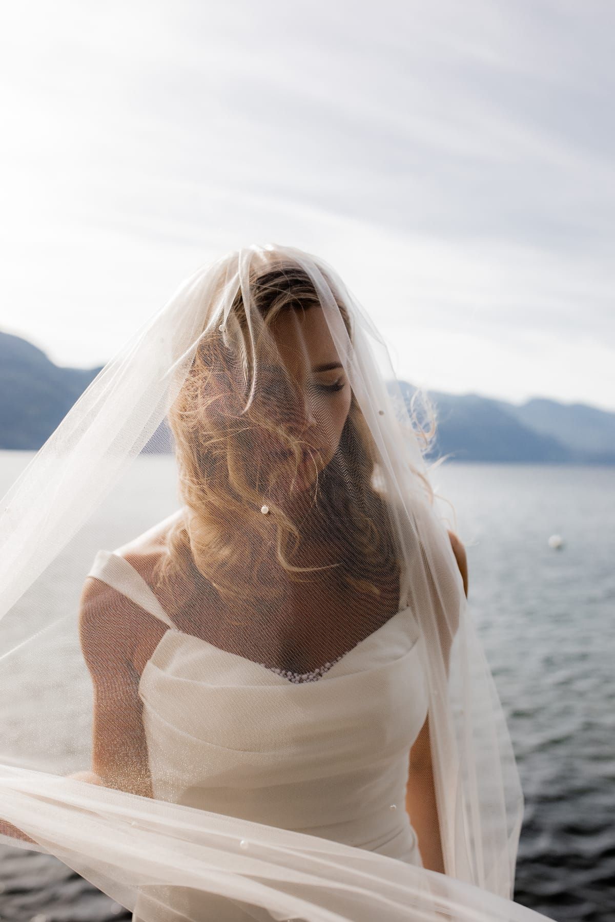 Bride with flowing veil by mountain lakeside