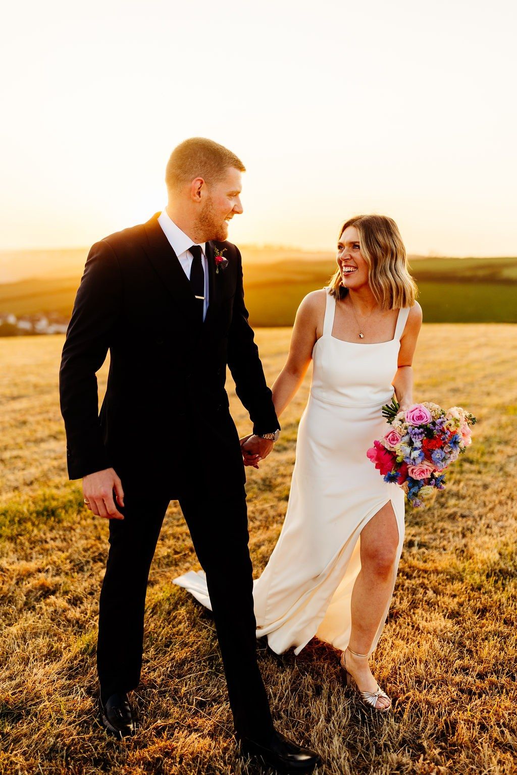 Bride and groom holding hands in a golden field at sunset