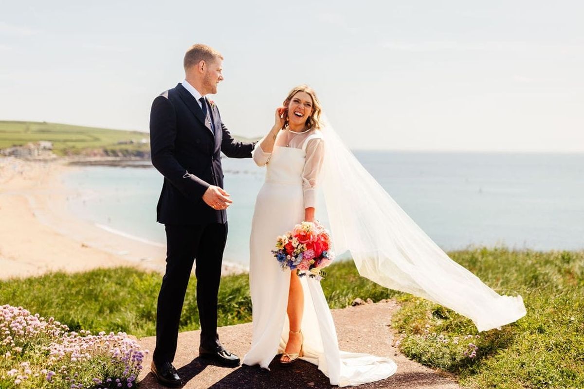 Joyful bride and groom celebrating with bouquet by coastal cliffs at golden hour