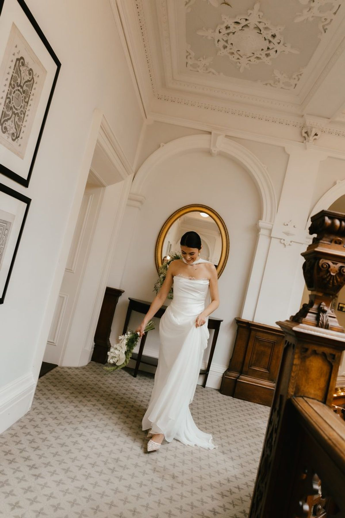 Bride with bouquet by gold mirror in elegant hallway