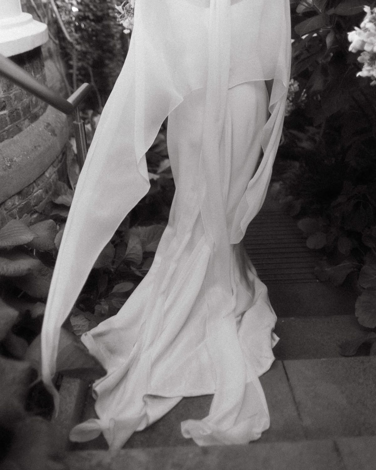 Flowing silk wedding dress and veil on garden steps, black and white