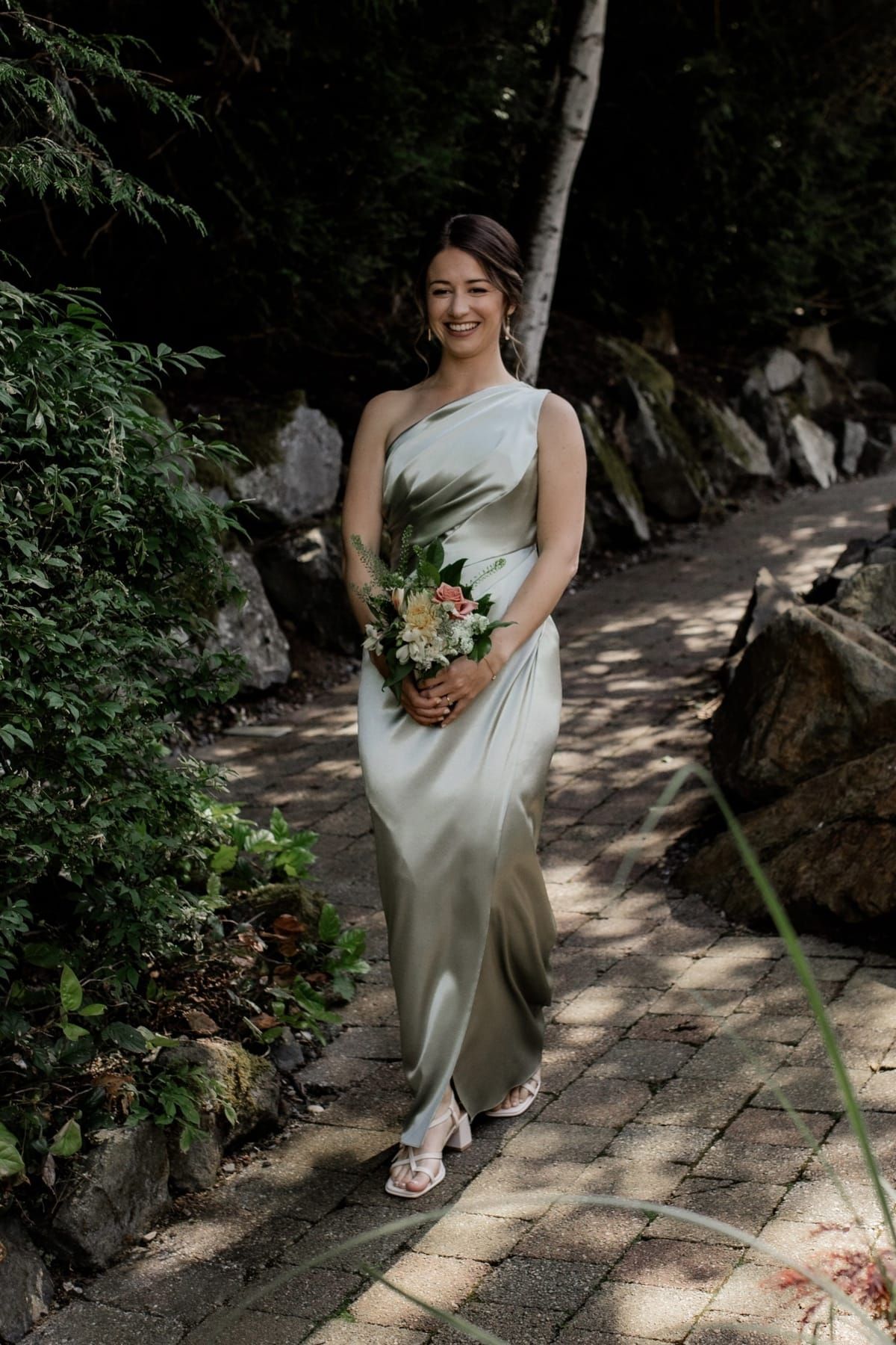 Bride in elegant one-shoulder sage green dress in natural outdoor setting