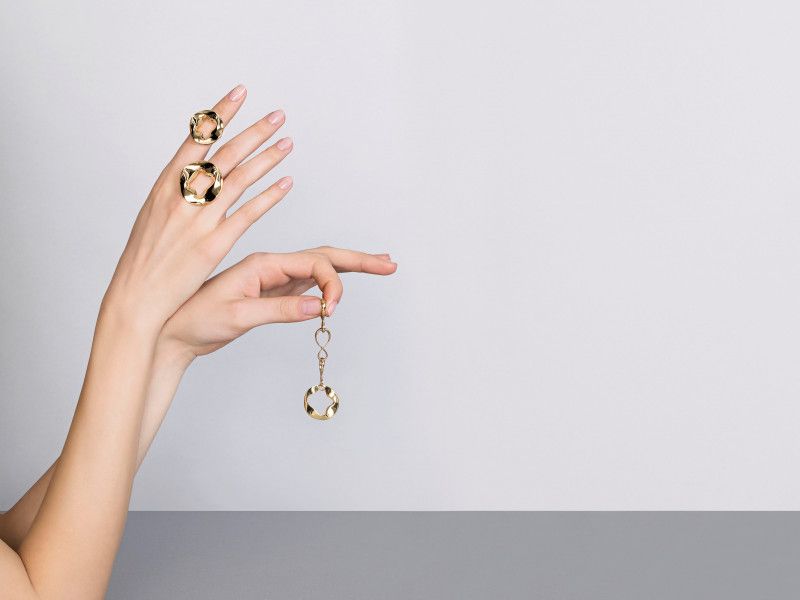two hands holding two golden rings and a golden pendant