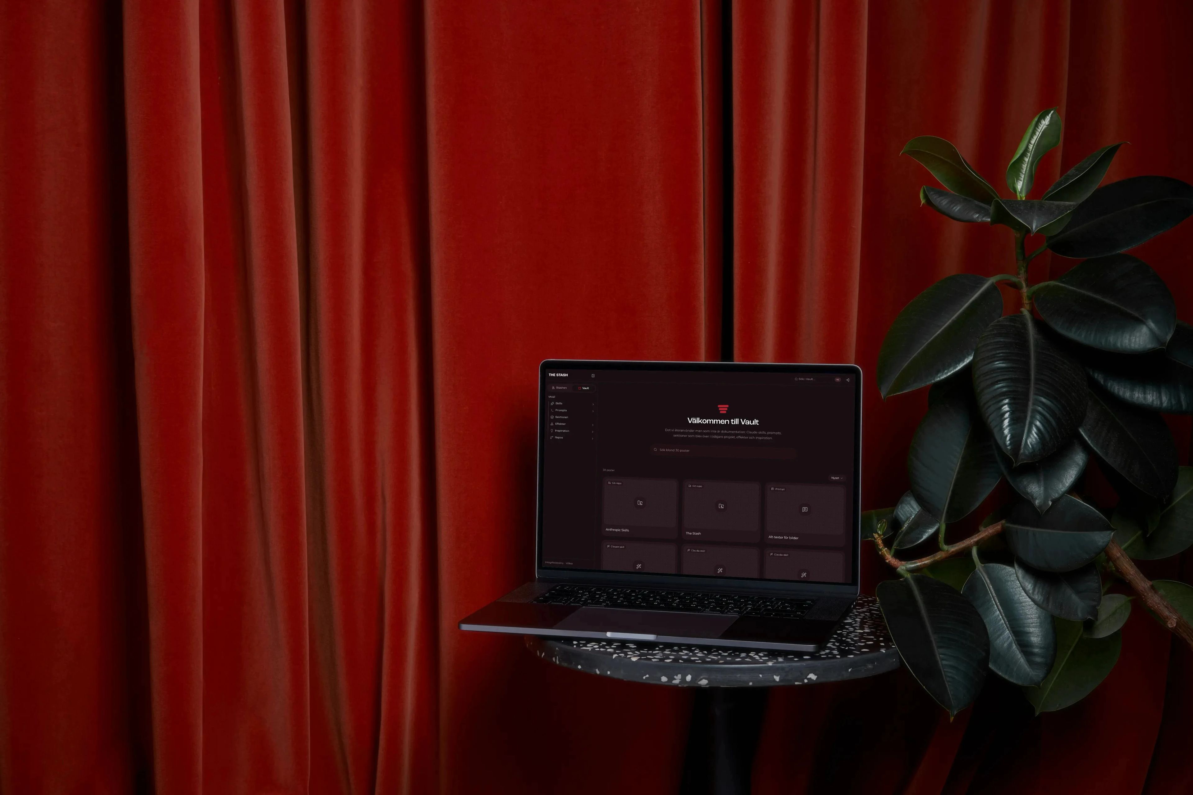 The dark Vault in The Stash on a MacBook on a terrazzo stool, in front of a red curtain
