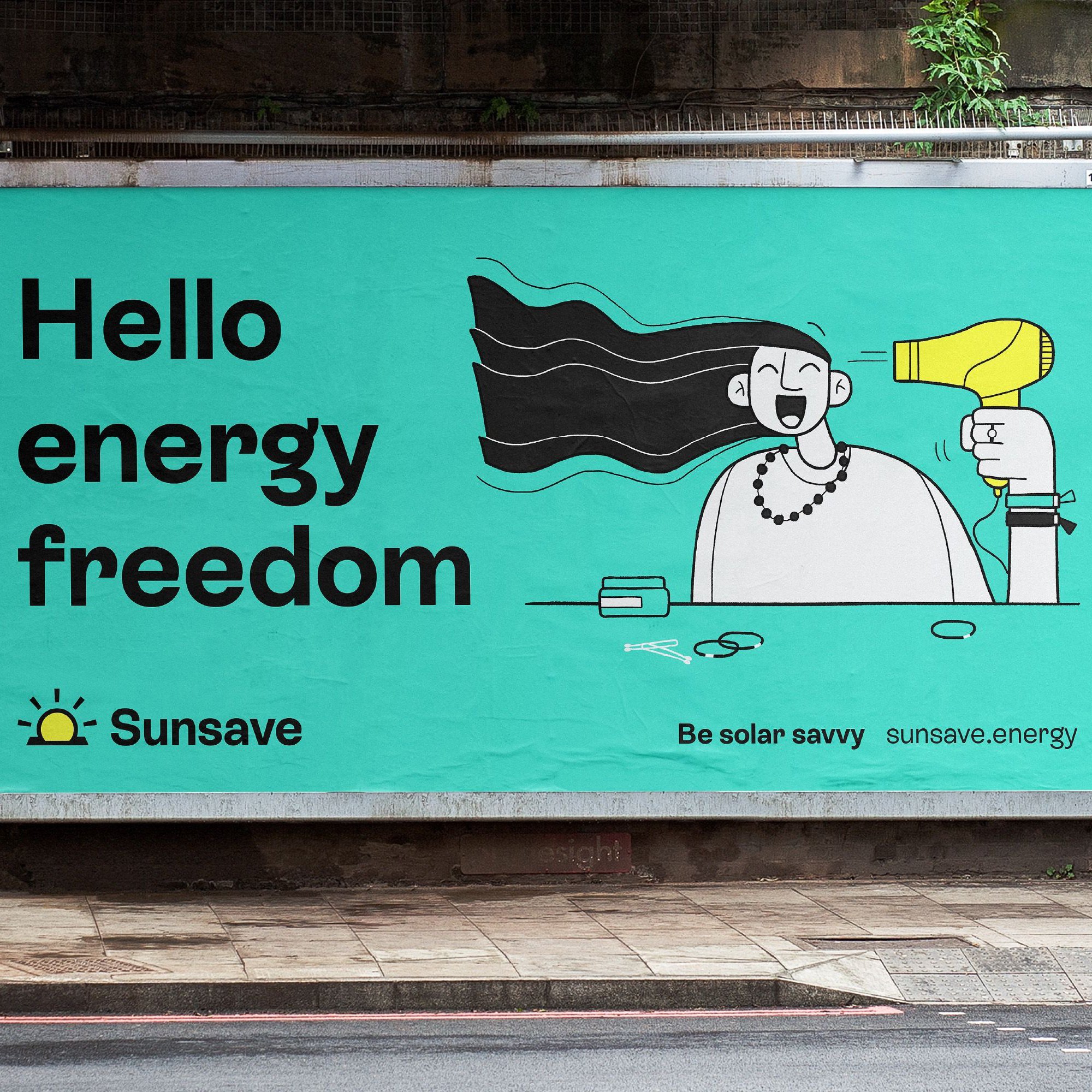 Billboard advert for the brand SunSave is displayed next to the side of a road. The copy on screen reads “Hello energy freedom” and features a filled line illustration of a character who is drying their hair with a yellow hairdryer. The text and illustration is set on a teal background within the billoard frame