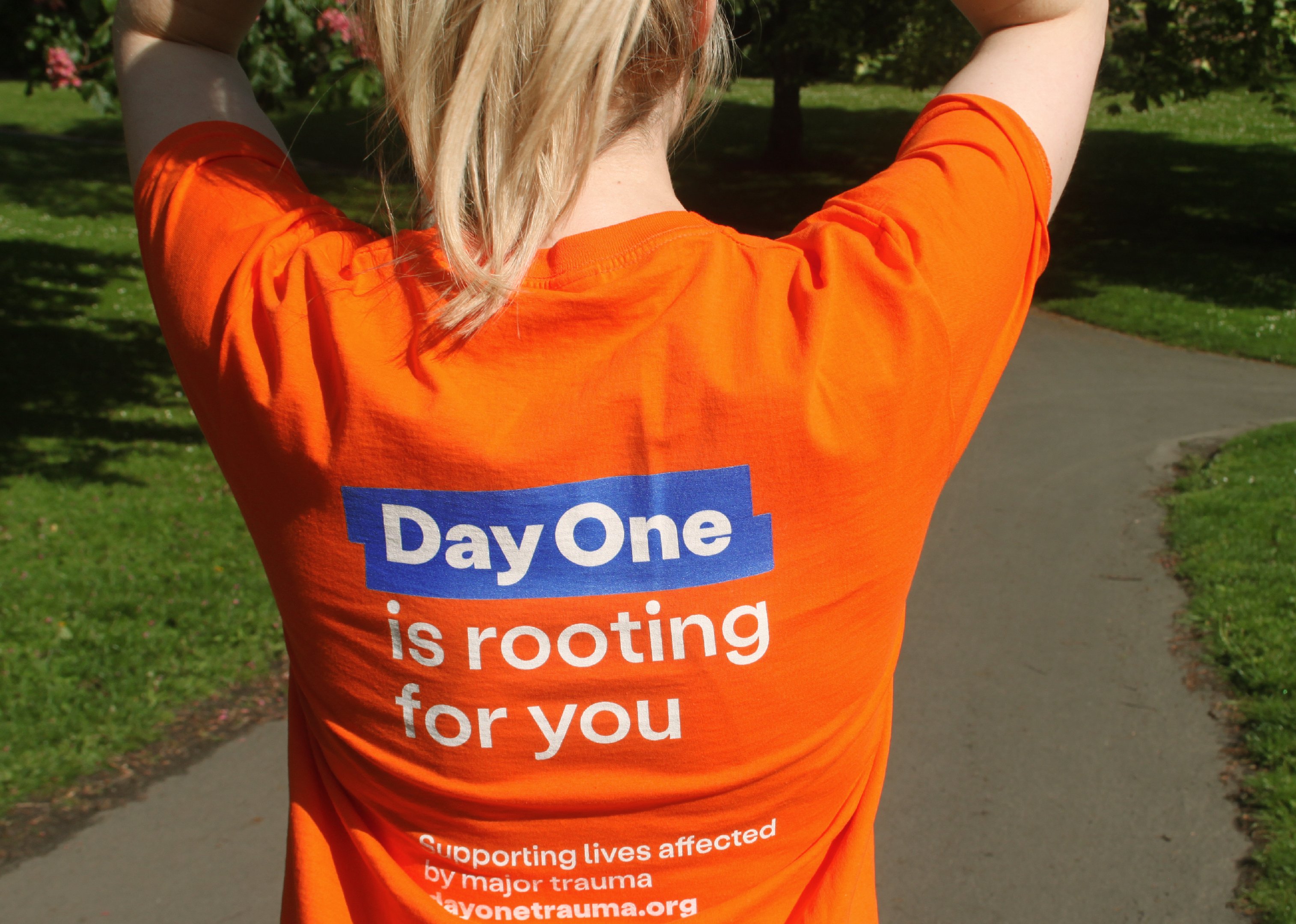 Image of a fundraiser wearing a Day One shirt is seen in a close up at the park. The writing on the back of her shirt reads: "Day One is rooting for you"