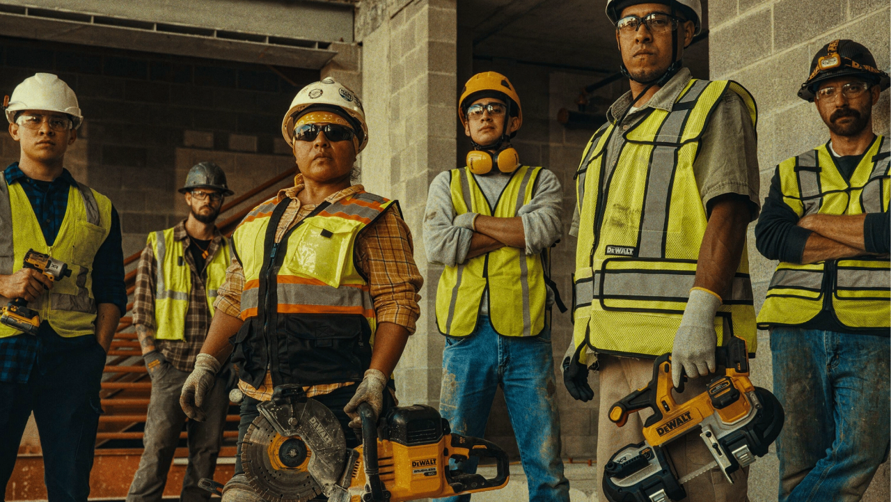 Construction workers in safety gear holding DeWalt tools at a construction site.