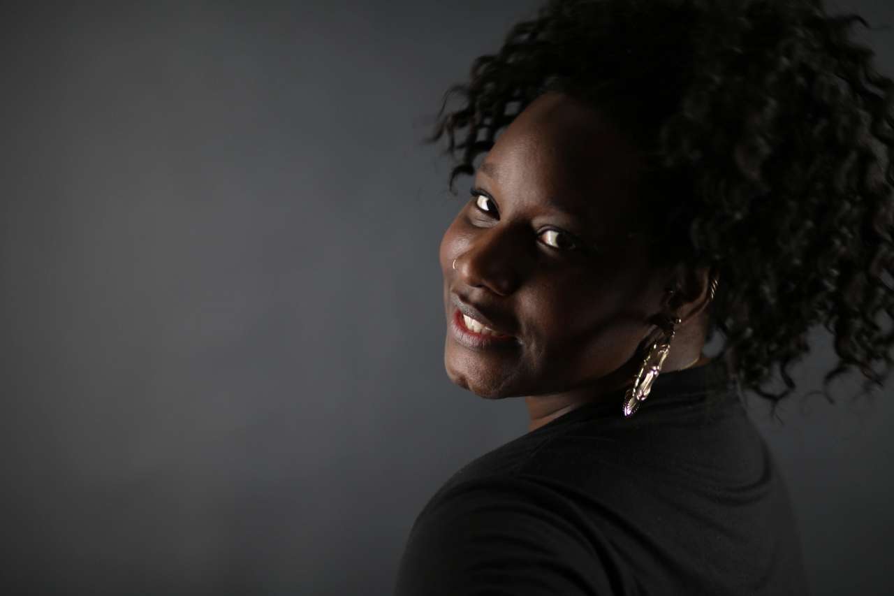 Portrait of a person with curly hair and earrings, smiling over their shoulder.