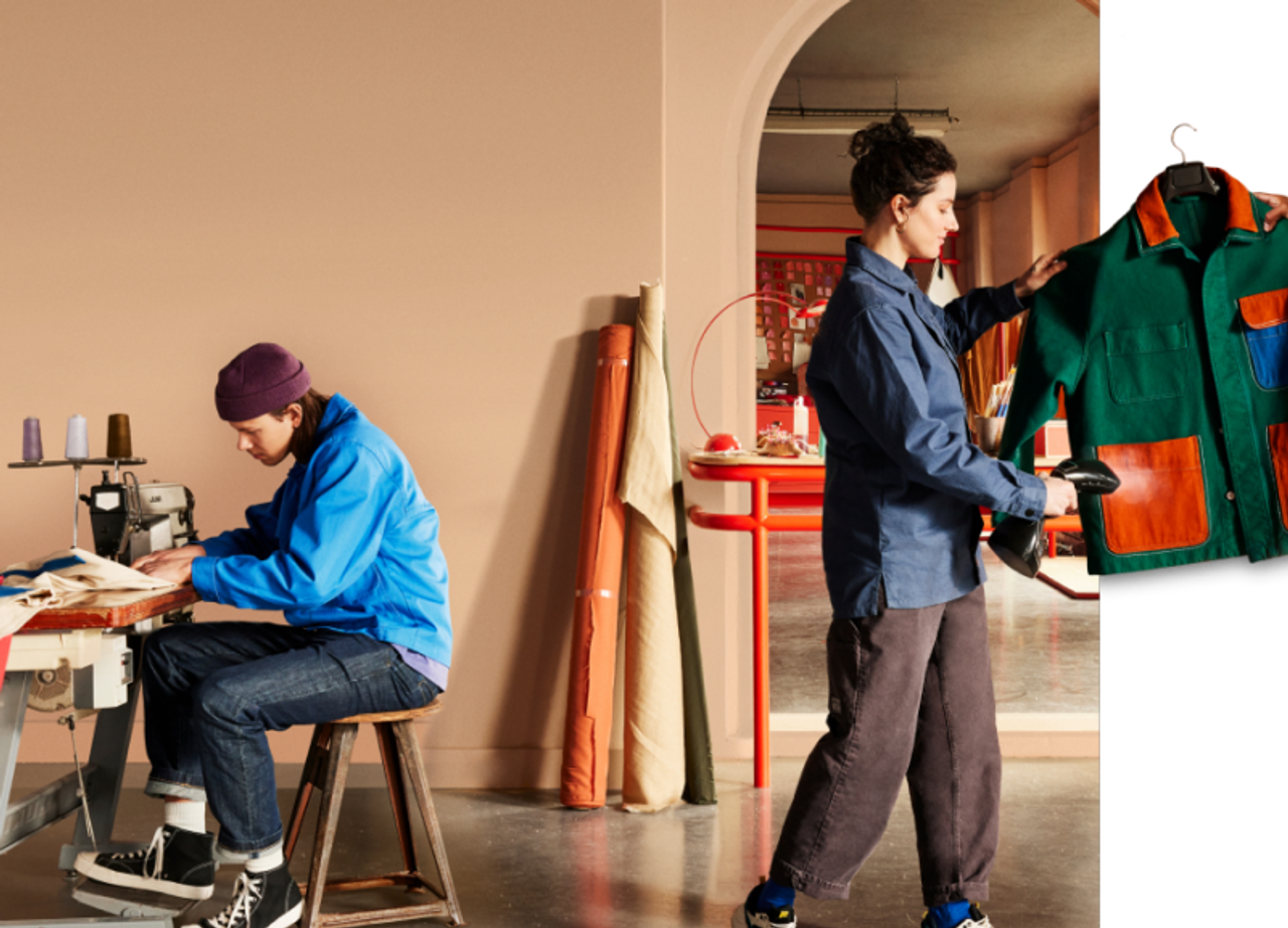 Creative workspace with two people; one sewing, the other holding a colorful jacket.