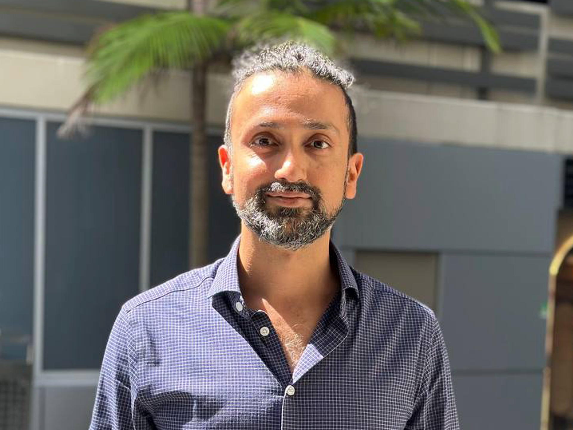 a man with a beard and a blue shirt is standing in front of a building .