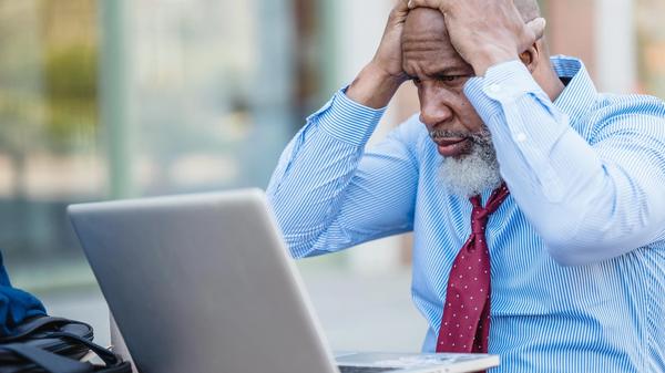 Man sitting at a laptop with his head in his hands looking stressed. 