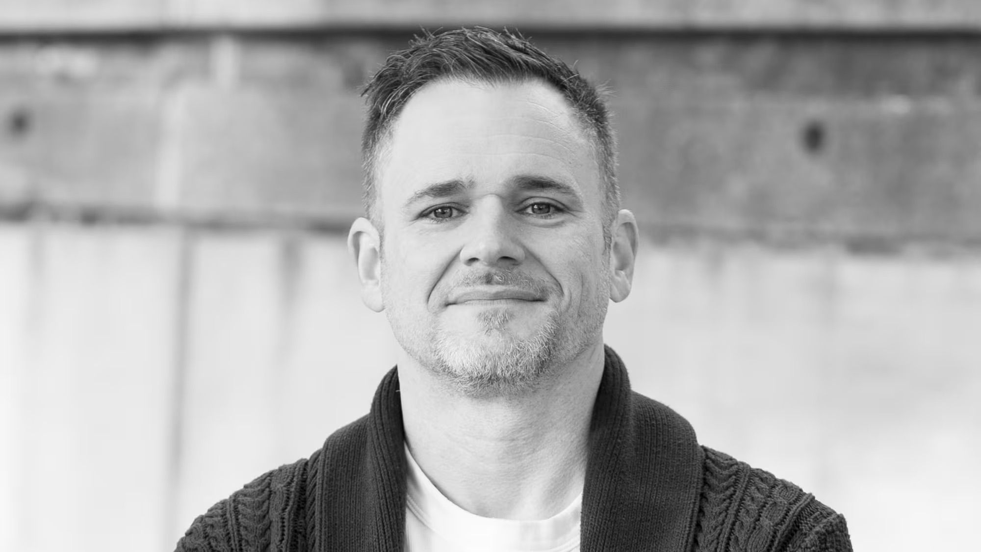Black-and-white portrait of a man wearing a dark cardigan over a white shirt.