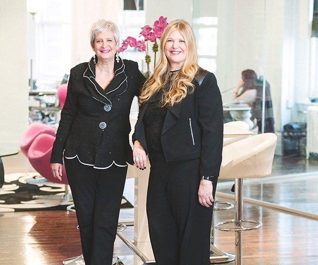 Terri and Sandy standing together in a salon with pink orchids in the background.