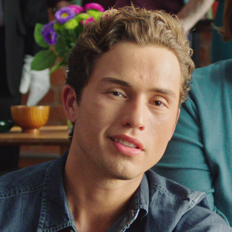 Portrait of a young man wearing a denim shirt in an indoor setting.