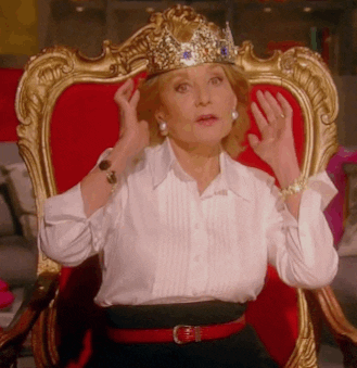 Older woman sitting on an ornate red-and-gold throne while adjusting a jeweled crown.
