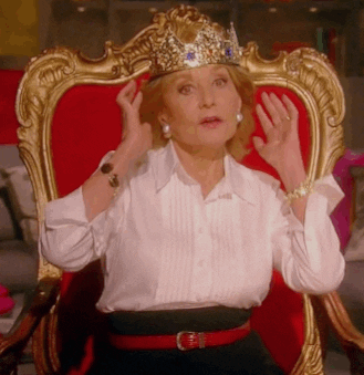 Older woman sitting on an ornate red-and-gold throne while adjusting a jeweled crown.