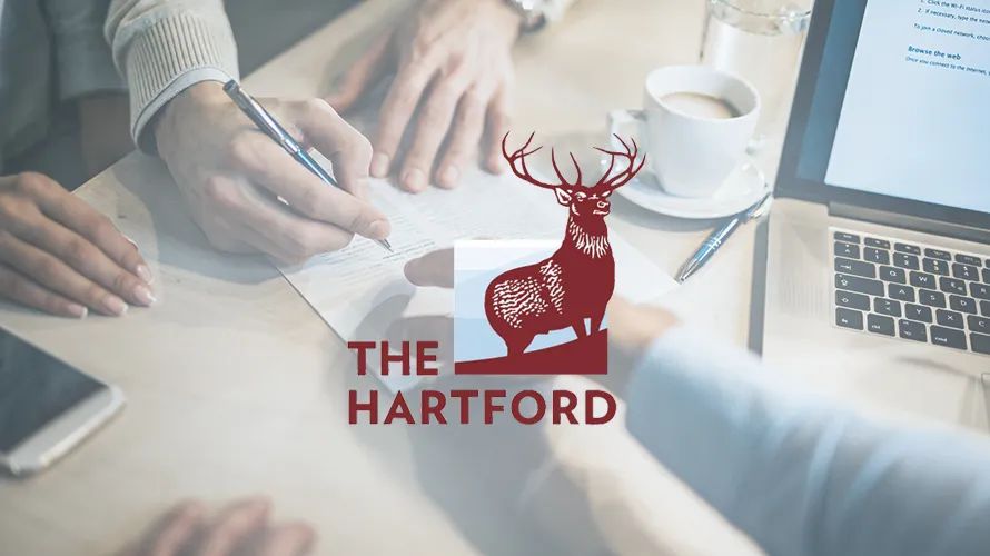 The Hartford Business Insurance logo featuring a red stag, overlaid on a photo of people reviewing documents at a table with a laptop and coffee.