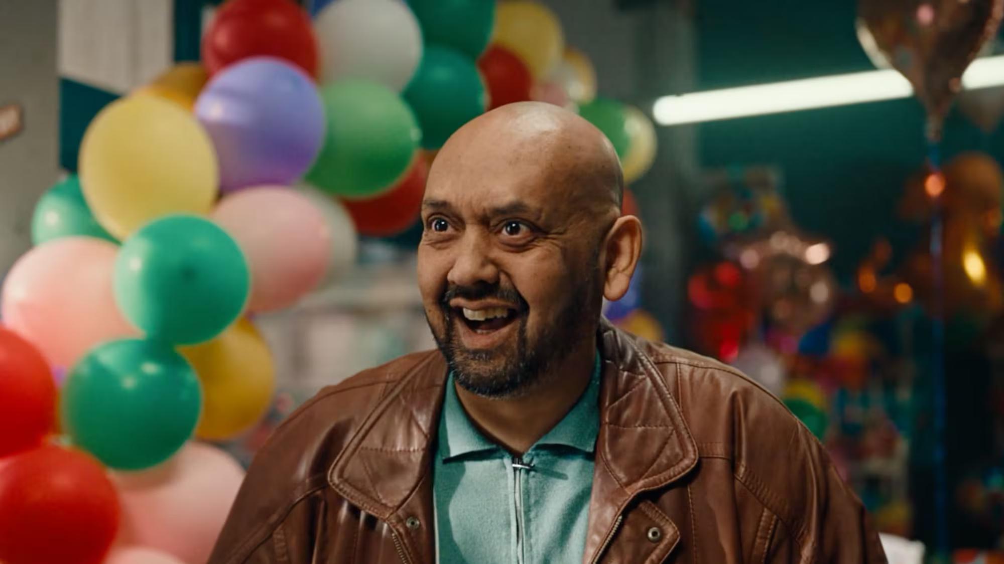 Man smiling at a colorful, balloon-filled event in an advertising campaign scene.