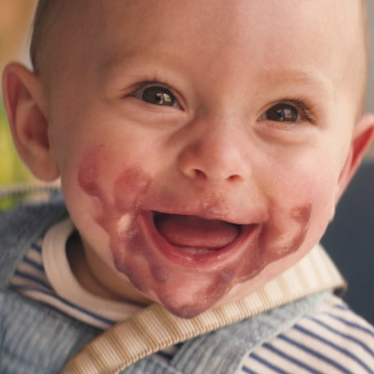 Smiling baby with baby food smeared around the mouth and cheeks.