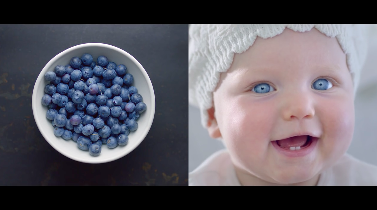 Smiling baby wearing a white knit hat beside a bowl of fresh blueberries.