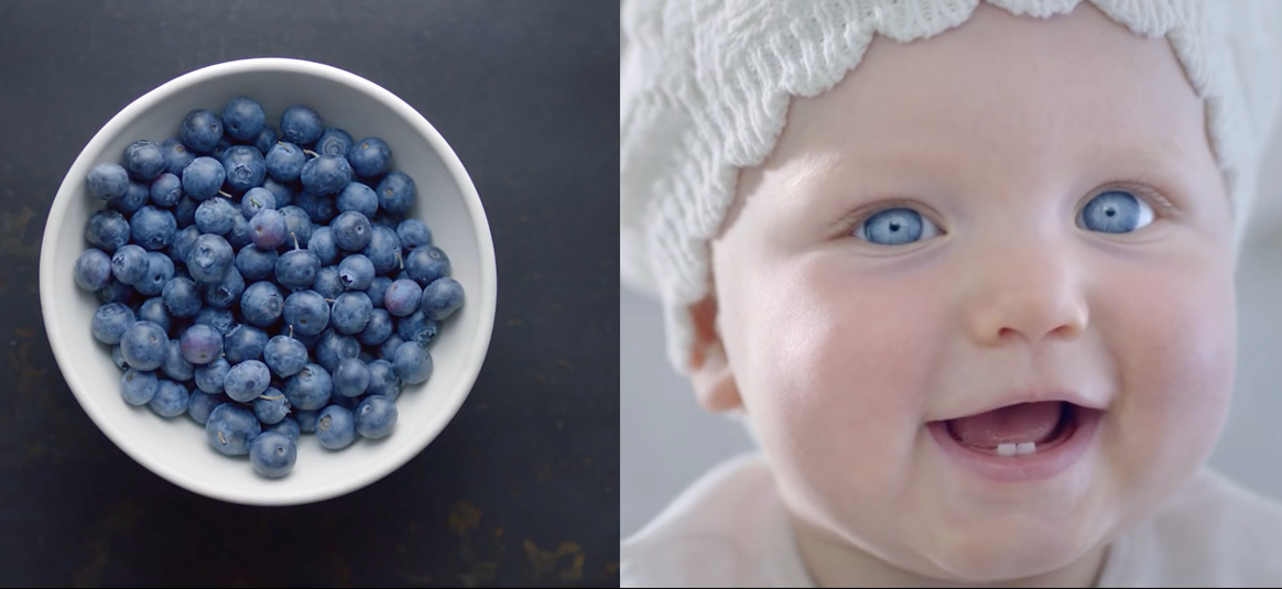 Smiling baby wearing a white knit hat beside a bowl of fresh blueberries.