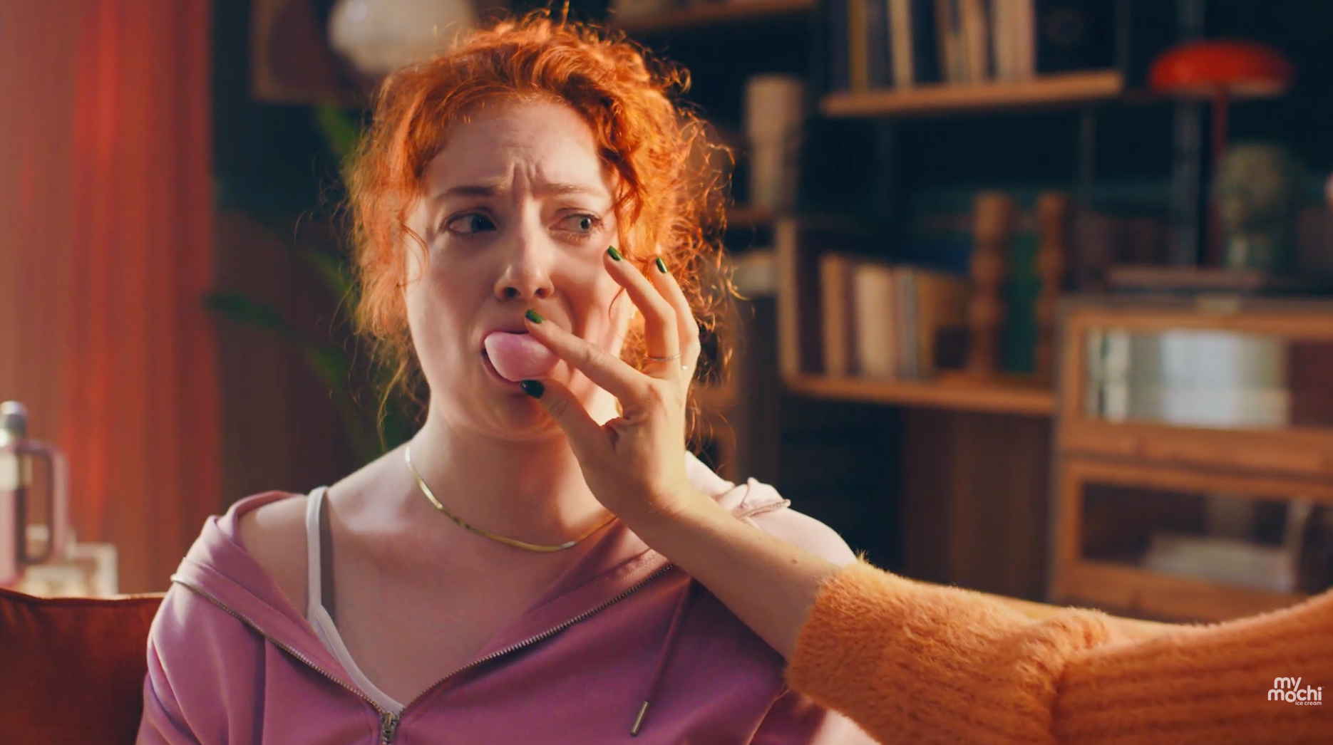 Woman reacts with a surprised expression as another person offers her a pink ice cream bite in a My/Mochi ice cream campaign scene.