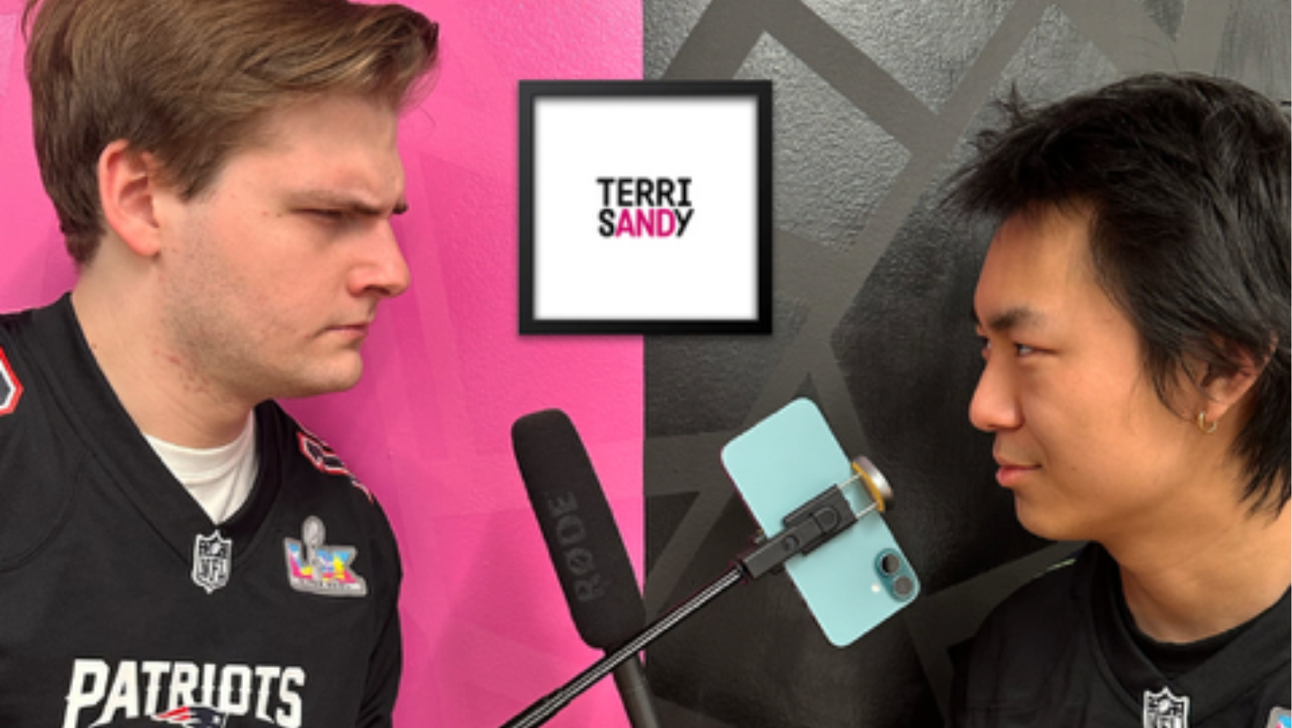 Two men wearing New England Patriots jerseys face each other during an interview with a smartphone mounted on a microphone stand.