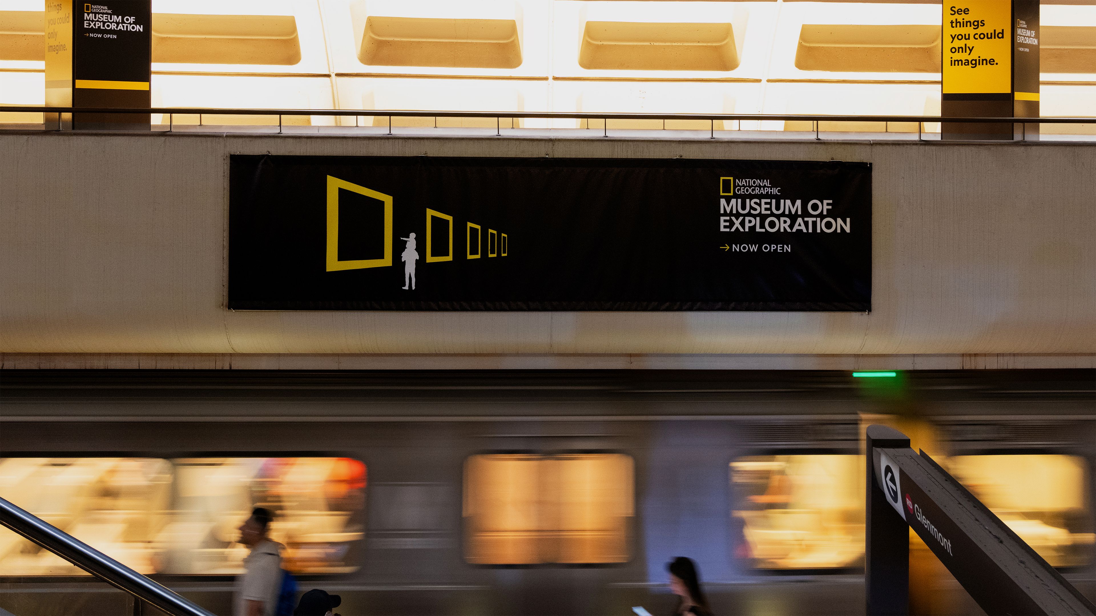 National Geographic Museum of Exploration subway banner featuring yellow frames and a silhouette, with a moving train below.