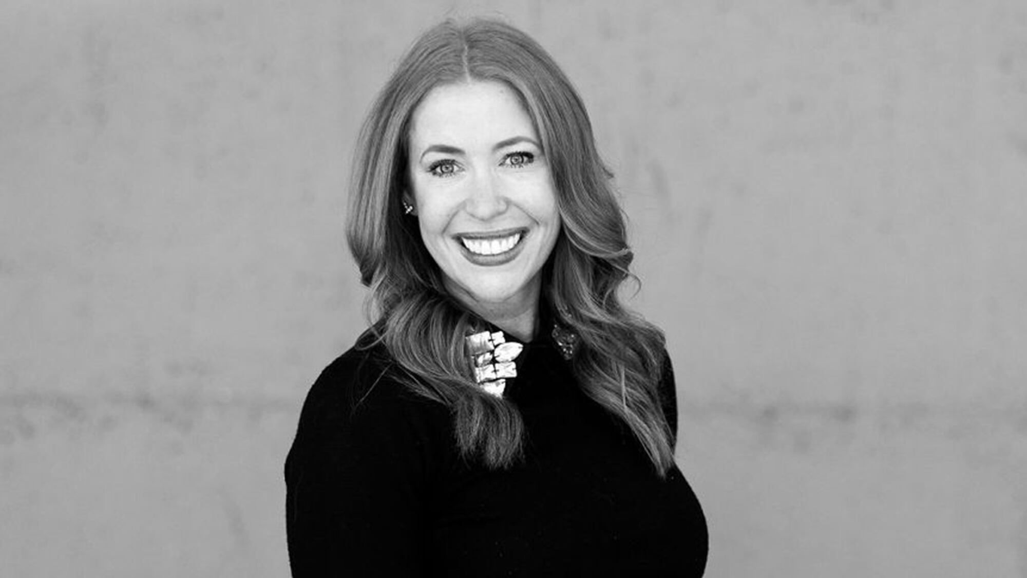 Black-and-white professional portrait of Peyton Sutton smiling in a black outfit against a neutral background.