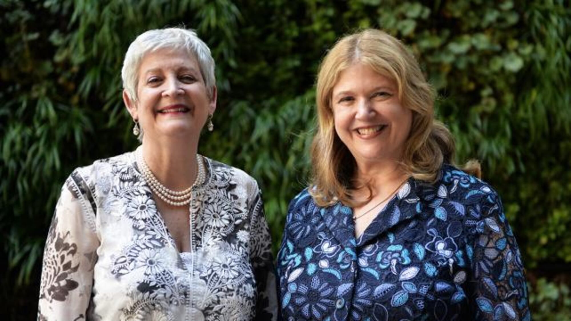 Terri and Sandy standing together in front of lush green foliage.