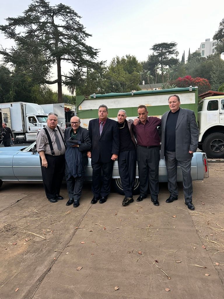 Steve Schirripa and fellow actors pose beside a vintage blue car on the set of a Freshpet commercial.