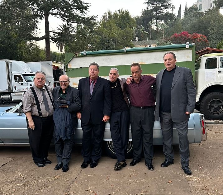 Steve Schirripa and fellow actors pose beside a vintage blue car on the set of a Freshpet commercial.