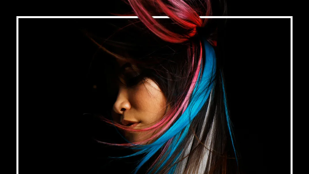Close-up portrait of a woman with dark hair accented by bright pink and blue streaks.