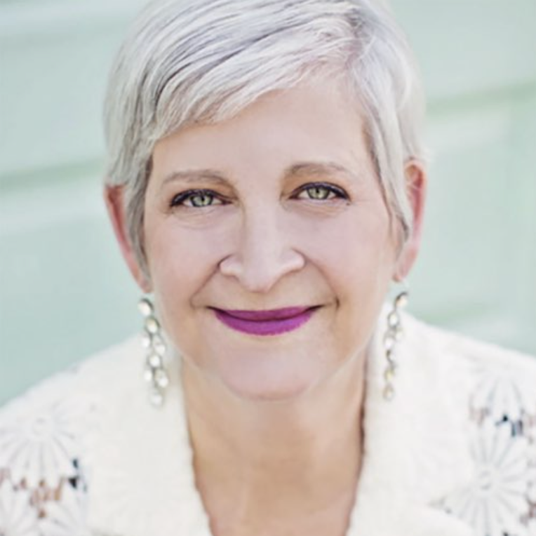 Professional headshot of Sandy with short silver hair and dangling earrings.